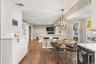 Eat in kitchen area with bar height seating. Wood-finish flooring throughout, recessed lighting, and a modern globe chandelier. Built in white cabinet