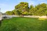 Expansive backyard featuring a manicured lawn, established trees, a raised deck, and a white privacy fence