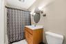 Oak finish vanity with a white countertop, oval mirror, wall-mounted light fixture, and white floor tiling