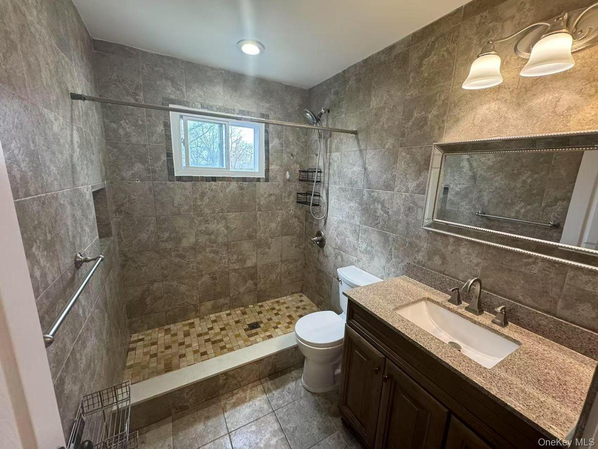 Full bath featuring vanity, tasteful backsplash, tile walls, a tile shower, and toilet