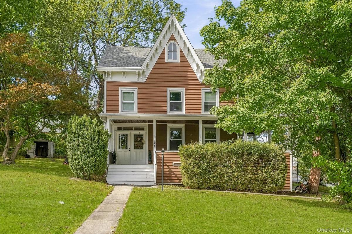 Gabled roofline, front porch, double entry doors, front lawn, and mature trees