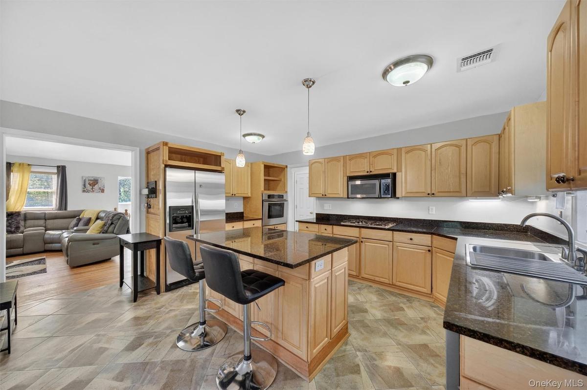 Kitchen featuring wood-finish cabinetry, dark countertops, a stainless steel refrigerator, a built-in microwave, and a center island with pendant ligh