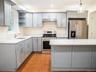 Kitchen featuring a sink, under cabinet range hood, open shelves, gray cabinetry, and appliances with stainless steel finishes