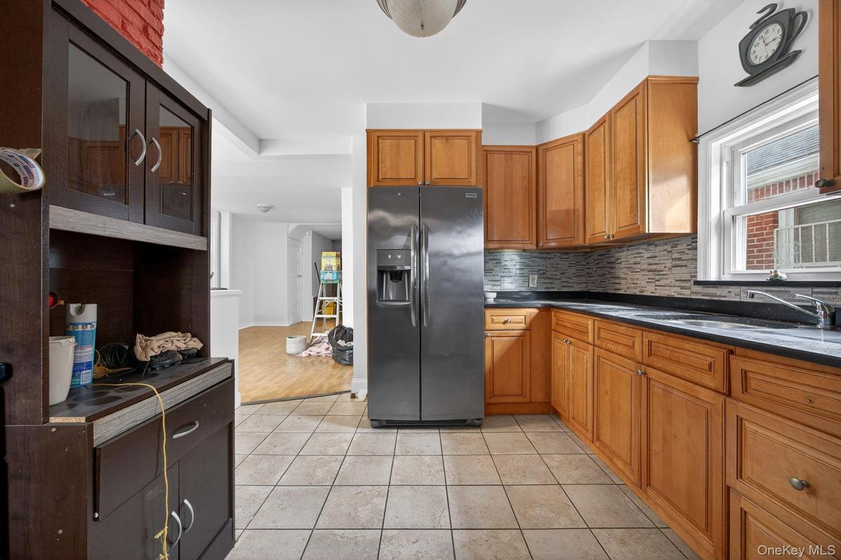 Kitchen featuring brown cabinetry, stainless steel refrigerator with ice dispenser, light tile patterned floors, and decorative backsplash