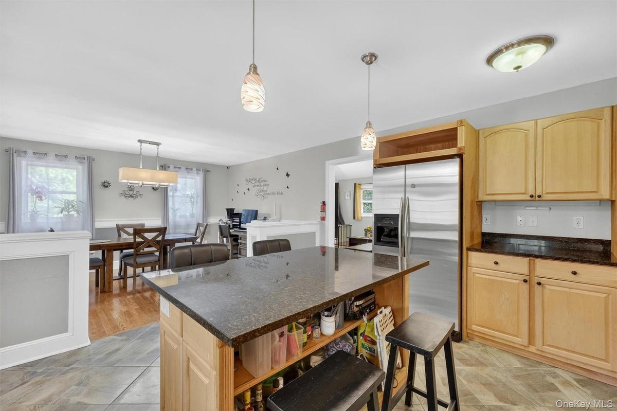 Kitchen featuring a center island with countertop seating, stainless steel refrigerator, wood-finish cabinetry, and dark countertops