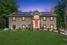 Stucco exterior with stone-look corner accents, solar panel array, arched entry window, red front door, and established landscaping