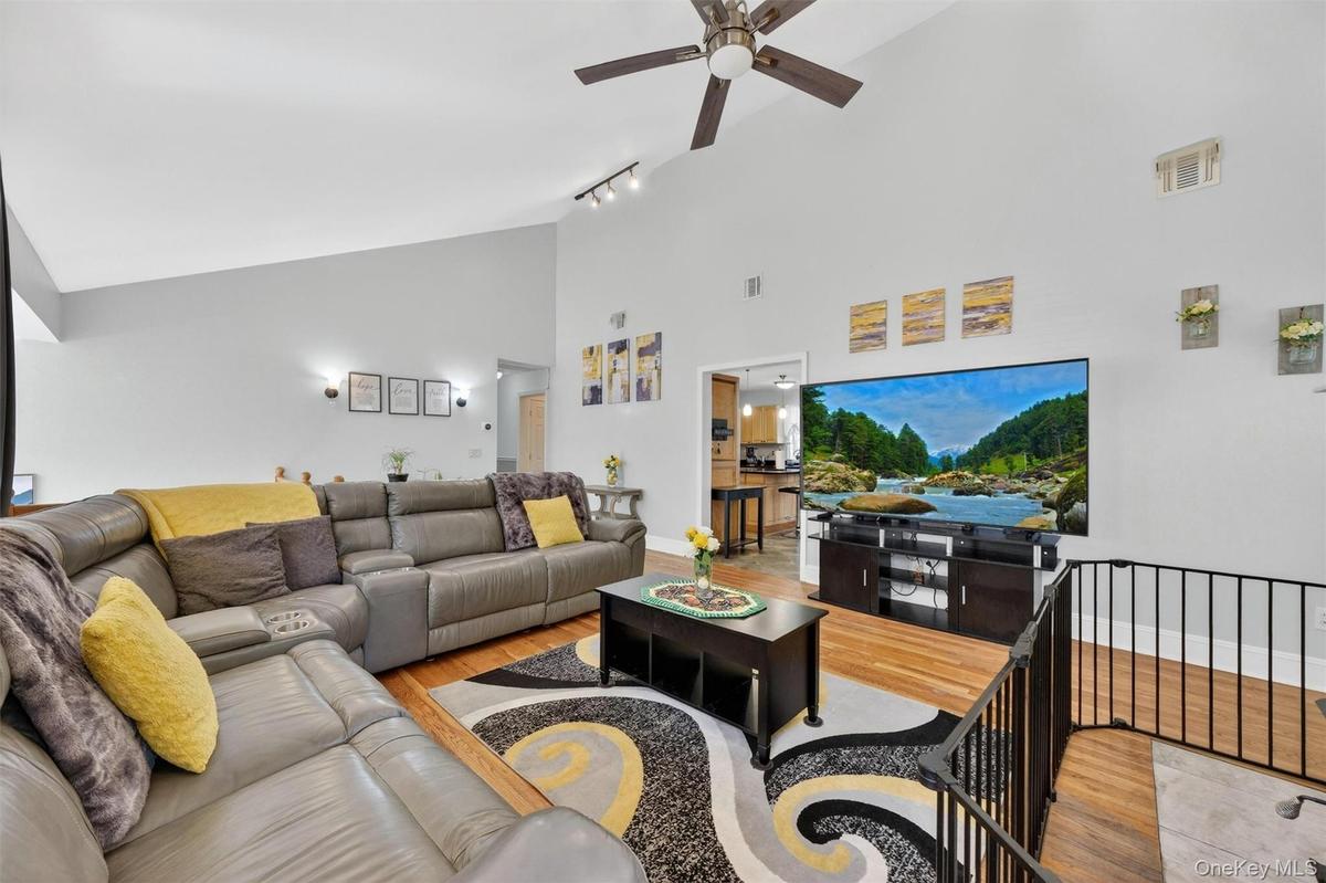 Vaulted ceilings with a ceiling fan, track lighting, wood-finish flooring, and a black metal railing