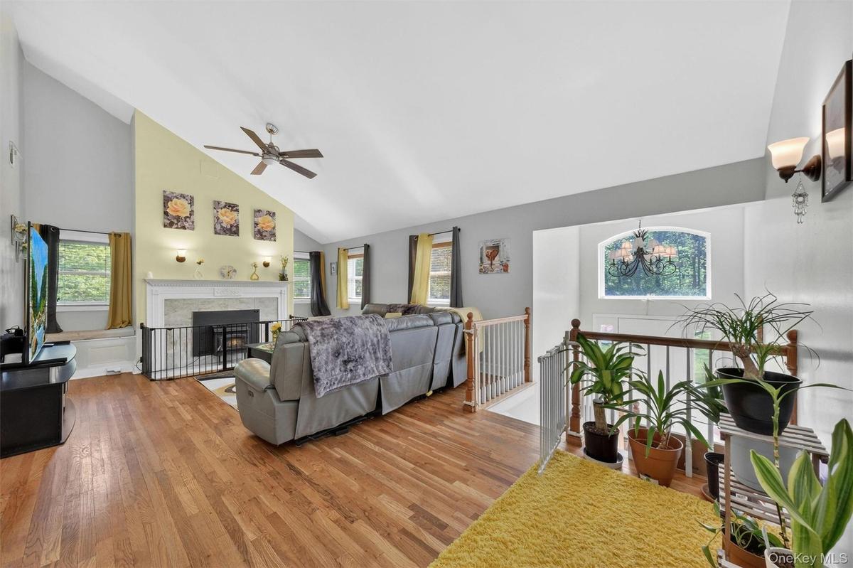 Vaulted ceiling, hardwood flooring, fireplace with mantel, ceiling fan, and staircase with wooden railing