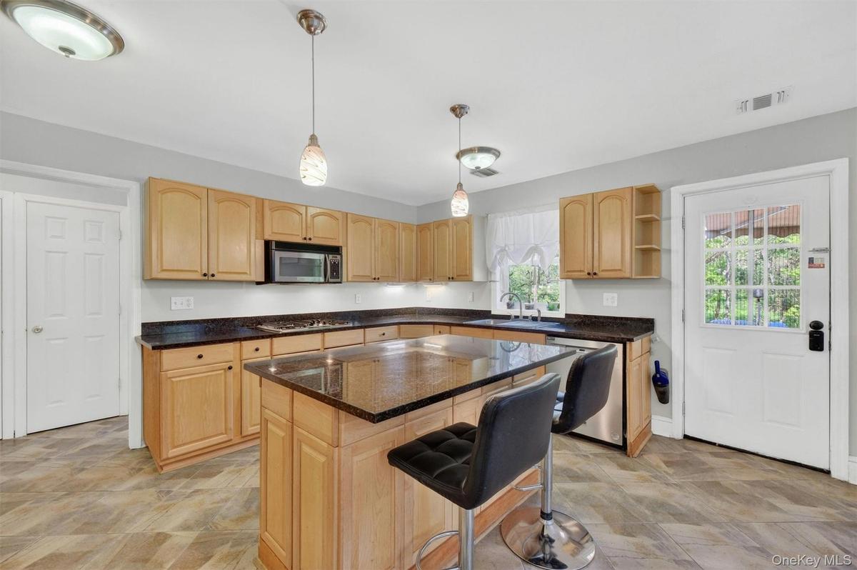Kitchen featuring wood cabinetry, dark countertops, a central island, stainless steel appliances, and wood-finish flooring