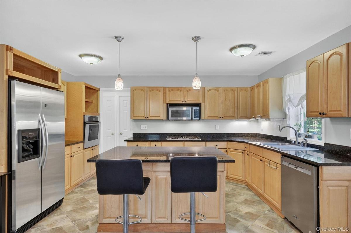 Kitchen featuring wood cabinetry, dark countertops, stainless steel appliances, a central island with pendant lighting, and patterned flooring