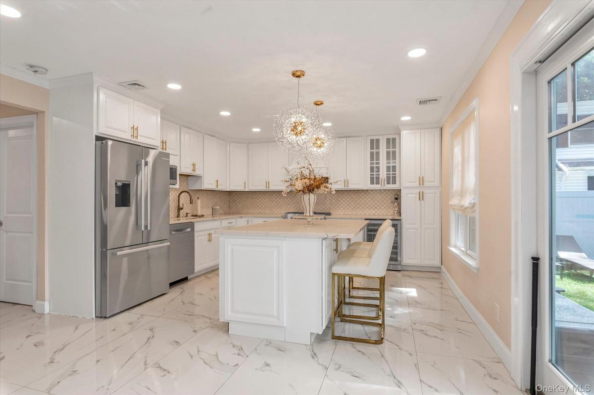 Cooks kitchen featuring white cabinetry, 2023 refrigerator, Bosch Dishwasher, Center island, Quartz Counters, Stainless steel appliances, beverage ref