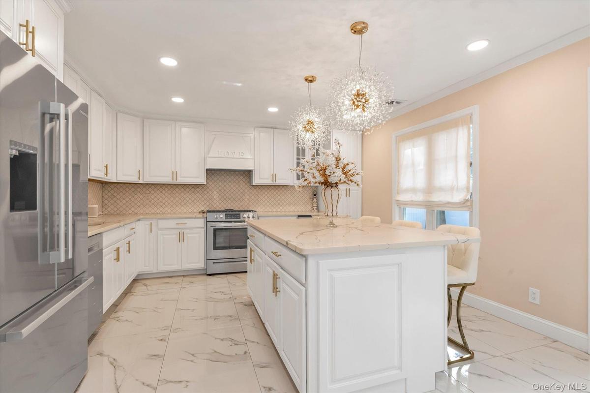 White cabinetry with gold-tone hardware and faucet taps, gas stove, stainless steel appliances, white quartz countertops, central island with storage,