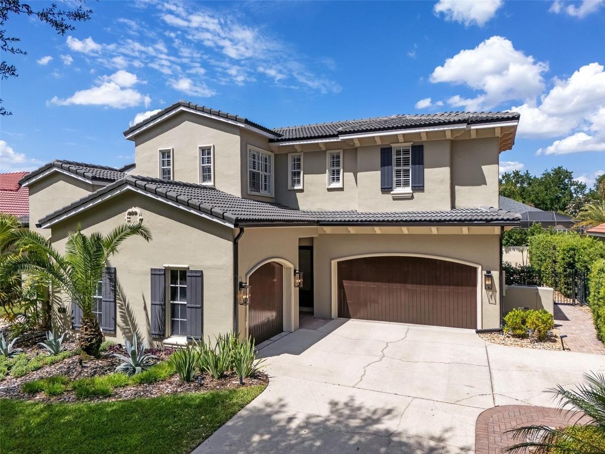 Two-story Mediterranean-style home with barrel tile roof, arched entry, paver driveway, and mature palm landscaping.