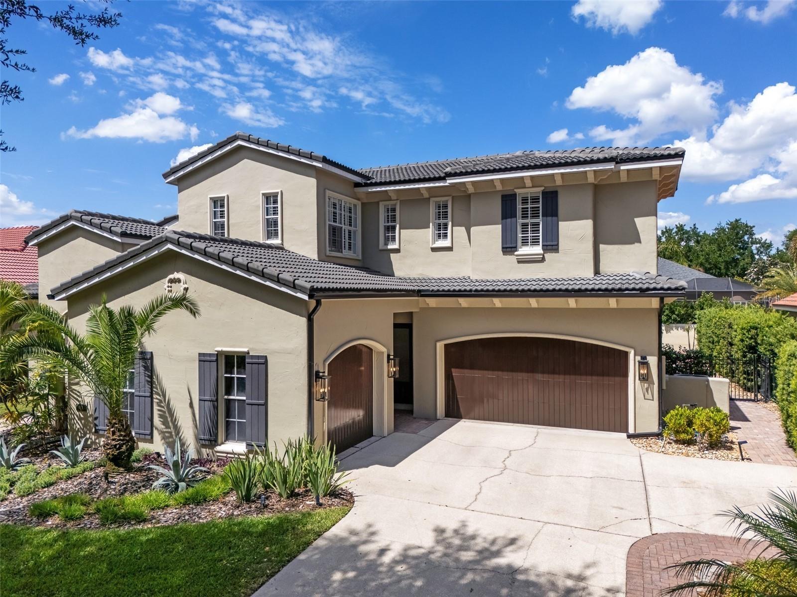 Two-story Mediterranean-style home with barrel tile roof, arched entry, paver driveway, and mature palm landscaping.