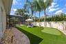 Artificial turf putting green with paver path and screen-enclosed pool beyond.