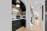 Arched entry to the pantry with black cabinetry, floating wood shelves, and stone countertops.