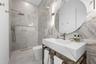 3rd Bathroom - Marble-look tile walls, console sink with brass frame, round mirror, and walk-in shower with brass fixtures.