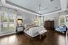 Tray ceiling with ceiling fan, dark wood flooring, and plantation shutters on multiple windows.
