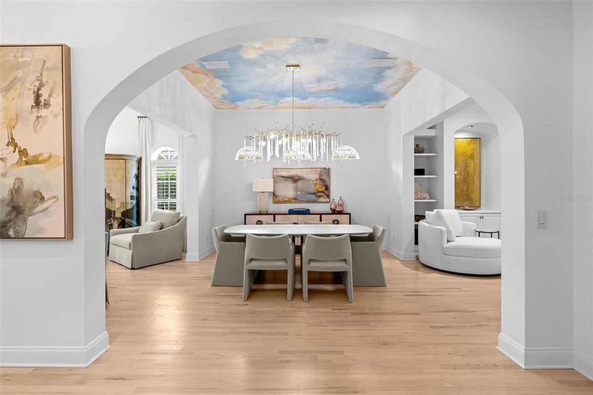 View through the arched entry to the dining room, showing the mural ceiling and chandelier.