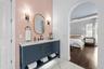 Navy vanity with stone top, pink herringbone tile wall, brass mirror, and arched view to the bedroom.