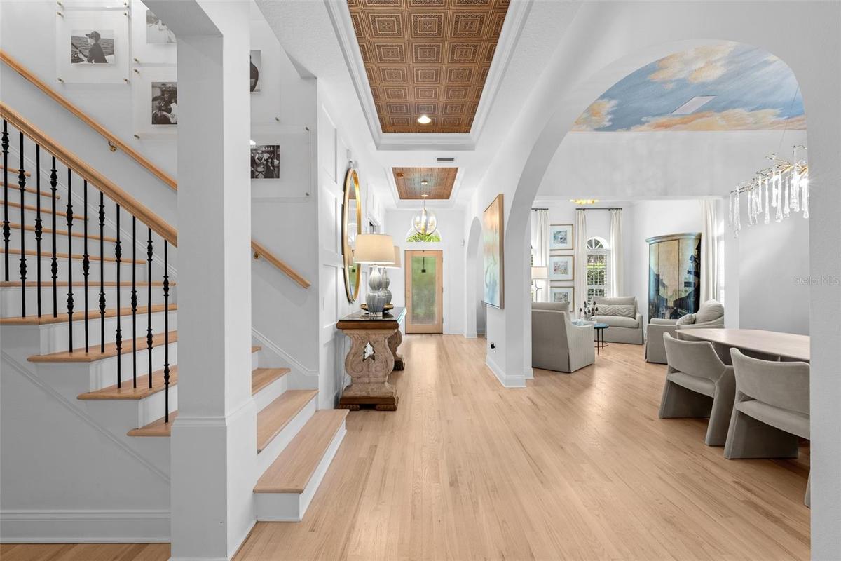 Foyer with light wood flooring, wood-inlay ceiling detail, staircase with iron balusters, and arched openings to the living spaces.