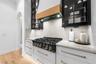 Six-burner gas cooktop, white tile backsplash, brass cabinet pulls, and stone countertops.