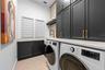 Laundry Room - Black shaker cabinets with brass pulls, front-load washer and dryer, and built-in louvered storage cabinets.