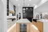 Island with built-in wine refrigerator, black pantry cabinetry, and glass-front uppers with pendant lighting.