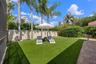 Backyard — Fenced yard with artificial turf, palms, and umbrella lounge seating.
