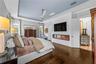 Tray ceiling, dark wood flooring, linear electric fireplace with mounted TV, and arched doorway.