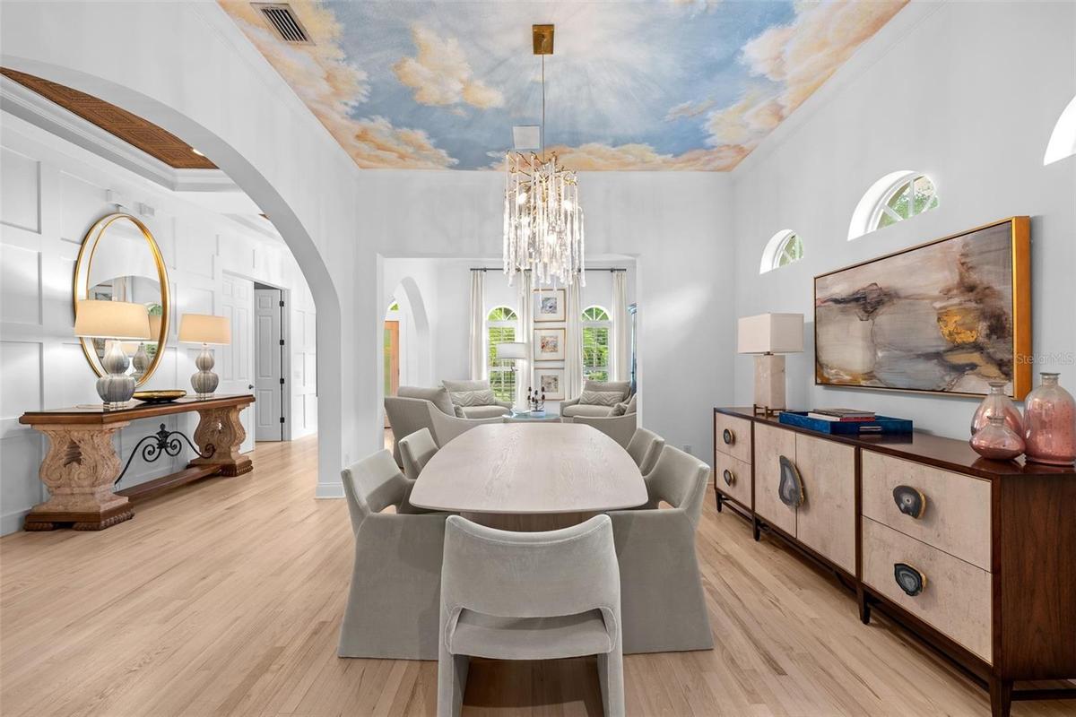 Formal dining space with a hand-painted sky ceiling mural, tiered chandelier, and built-in display shelving.