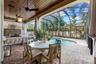 Covered lanai — Wood plank ceiling, ceiling fans, outdoor dining area, stone fireplace, and pool view.
