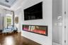 Linear electric fireplace beneath a mounted TV with an arched window and plantation shutters.