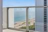 Glass balcony railing with a coastal backdrop featuring a sand beach and expansive ocean