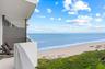 Private balcony with a curved design, featuring a partial privacy screen, and an expansive ocean and beach horizon