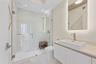 Glass-enclosed shower with full-height tile surround, illuminated vanity mirror, and a rectangular vessel sink with a single-handle faucet