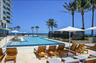 Resort-style pool area featuring multiple chaise lounges, structured cabanas, and ocean scenery