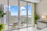 Sliding glass doors opening to a private balcony with glass railing, featuring a cityscape and water backdrop