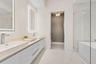 Dual vessel sinks with wall-mounted lighting, extensive vanity storage, and a glass-enclosed shower featuring a built-in tub