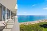 Expansive balcony with a curved concrete railing, large sliding glass doors, and direct oceanfront scenery