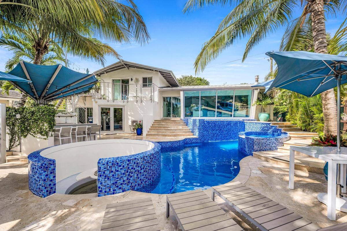 Backyard oasis featuring a curvilinear pool with blue mosaic tiling, integrated spa, and an elevated sundeck