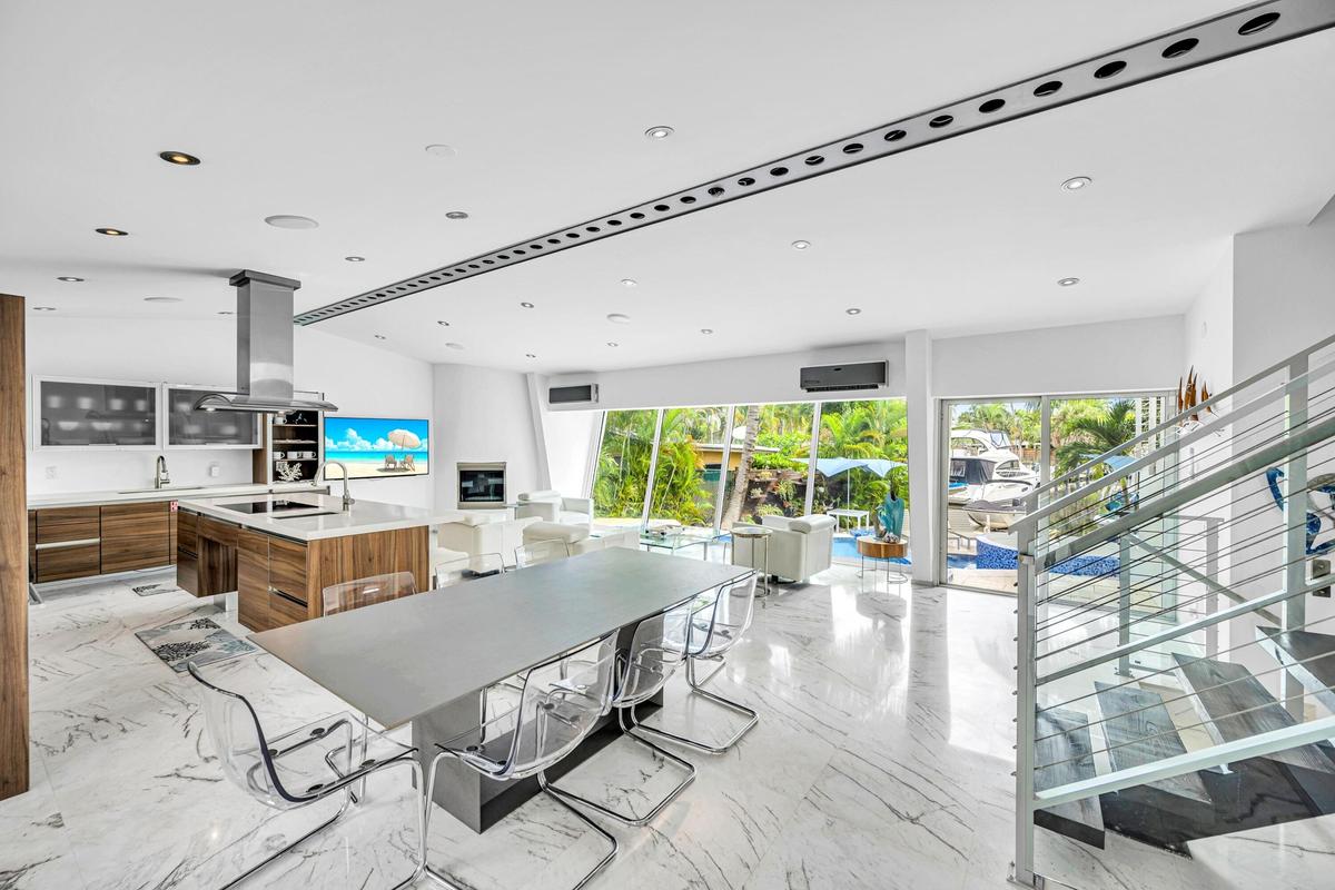 Open-concept living area with polished marble flooring, a modern kitchen island with wood-finish cabinetry, a stainless steel range hood, and a contem