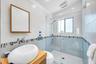 Glass-enclosed shower with a rainfall showerhead and a window, complemented by a vessel sink atop a wood-finish vanity, and a wall-mounted mirror with