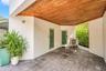 Covered patio featuring a wood-finish ceiling, light gray paver flooring, white stucco walls, and two exterior doors with frosted glass panels