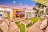 Outdoor entertainment space featuring a manicured lawn, string lighting overhead, built-in seating with wood-finish frames and cushioned upholstery, a