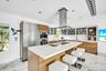 Sleek kitchen with a central island featuring dual sinks, a stainless steel range hood, built-in stainless steel appliances, wood-finish cabinetry, an