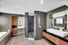 Curved tile shower enclosure with dark mosaic tile, dual wall-mounted sinks, wood-finish vanity with a vessel sink, recessed lighting, and a built-in 