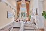 The foyer opens to a two-story travertine-tiled formal living area with dramatic fireplace and towering picture windows that frame the view of the poo