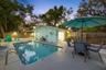 Evening lighting shows off the backyard’s resort-like setup, complete with heated pool, outdoor dining, BBQ area, and space to gather around the fire 