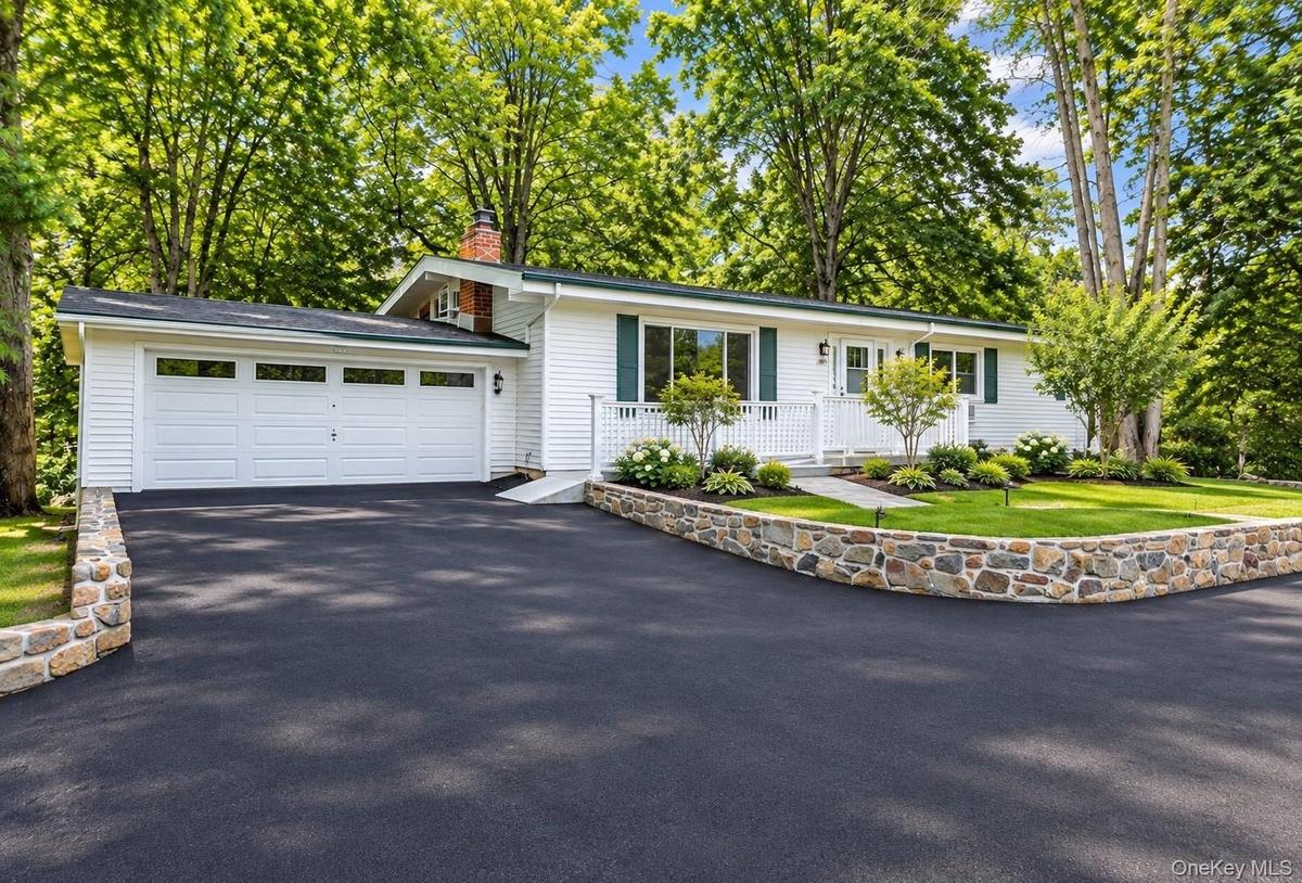 White siding exterior with a two-car garage, brand new asphalt driveway, and a stone retaining wall